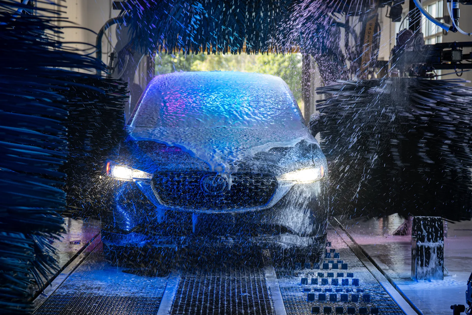 A car in the wash tunnel at Jilly's Car Wash, lit blue with soft-cloth washing